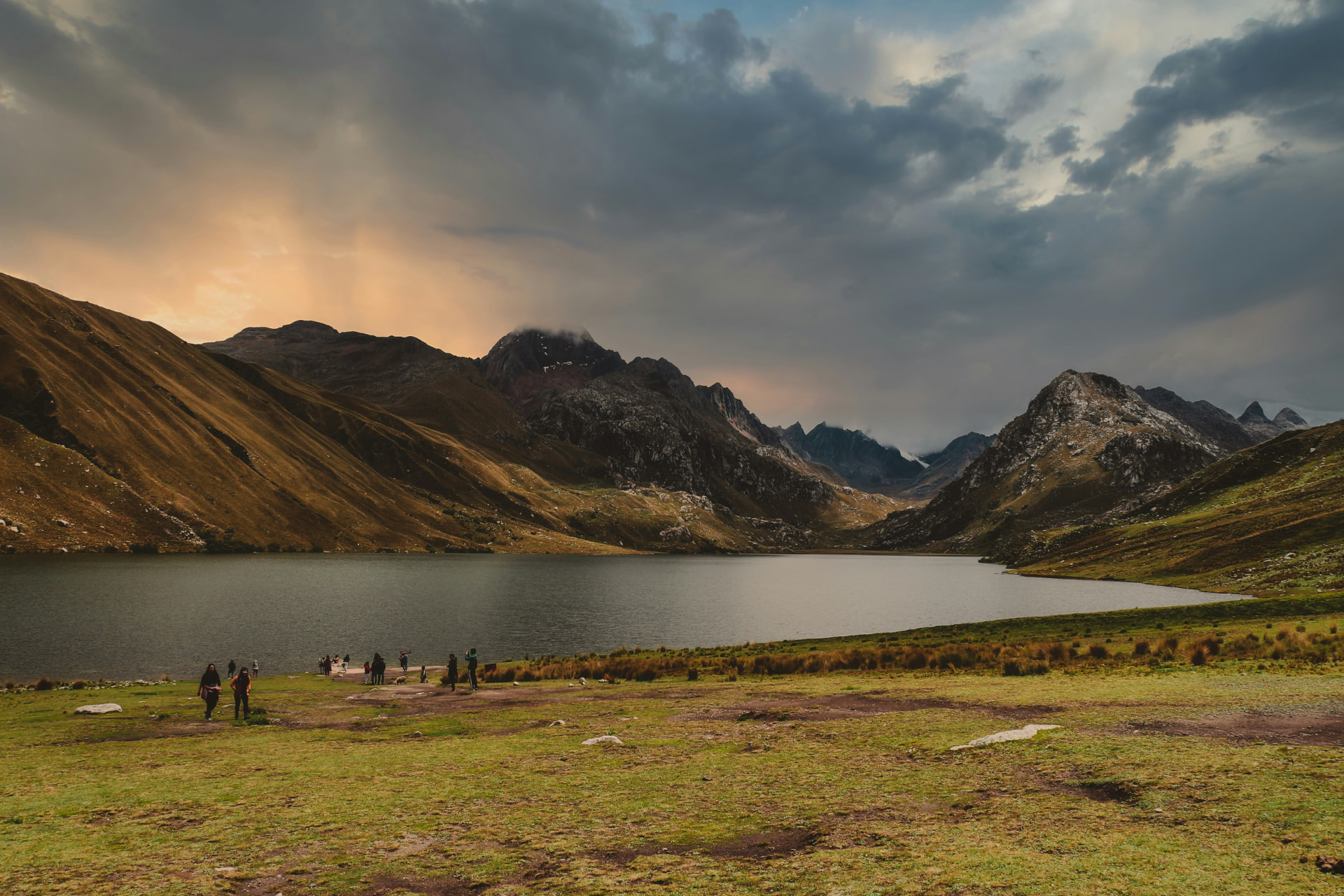 A mountain lake at dusk beneath a wide, clouded sky